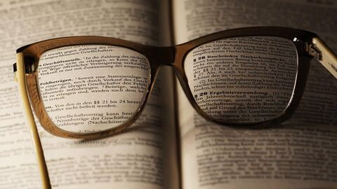 Brille liegt auf einem aufgeschlagenen Gesetzbuch.