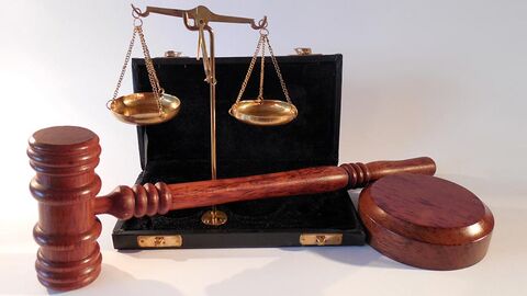 Waage und hölzerner Hammer vor einem kleinen Koffer.