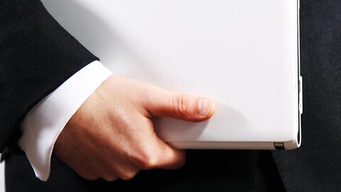 Hand hält eine Akte. Am Arm sind noch Manschetten und der Ärmel eines Jacketts zu sehen.