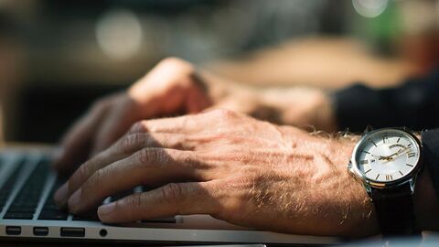 Zwei Hände, an einem Handgelenk eine Armbanduhr, tippen auf einer Tastatur.