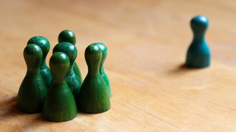 Sechs grüne Spielfiguren stehen dicht beieinander und eine weitere in deutlichem Abstand dazu.