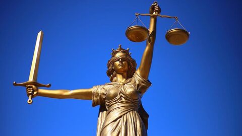 Goldfarbene Justitia-Statue steht vor einem blauen Hintergrund.