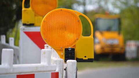 Im Vordergrund ist der Ausschnitt einer Straßensperre, im Hintergrund unscharf ein gelber Lastwagen zu sehen.