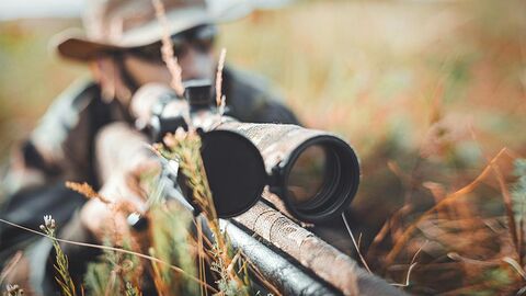 Jäger mit einem Gewehr mit Zielfernglas liegt im Gras.