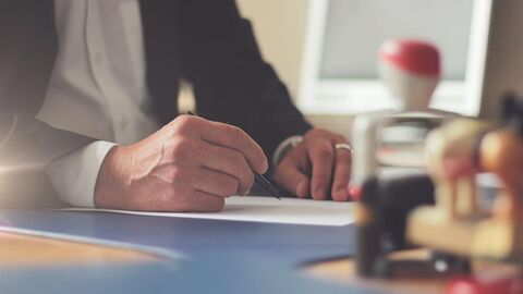 Büro (Symbolbild) Mann sitzt an einem Schreibtisch und schreibt.