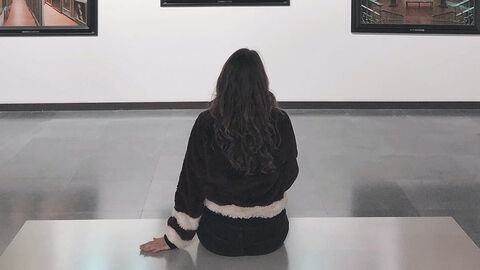 Galerie (Symbolbild) Frau sitzt auf dem Boden eines Raums und betrachtet Bilder an der Wand.