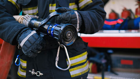 Feuerwehrmann steht vor einem Feuerwehrwagen mit einer Spritze in den Händen.