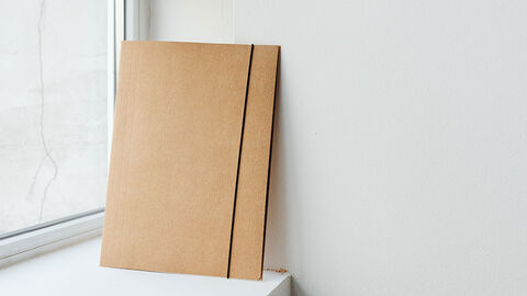 Geschlossene Vorgangsmappe lehnt auf einer Fensterbank gegen die Seitenwand.