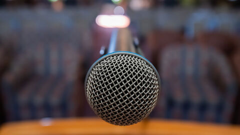 In der Bildmitte wird ein Mikrophon vor einem unscharfen Hintergrund gezeigt.