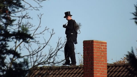 Schornsteinfeger balanciert über einen Dachfirst.