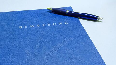 Auf einer blauen Mappe mit der Aufschrift -Bewerbung- liegt ein Kugelschreiber.