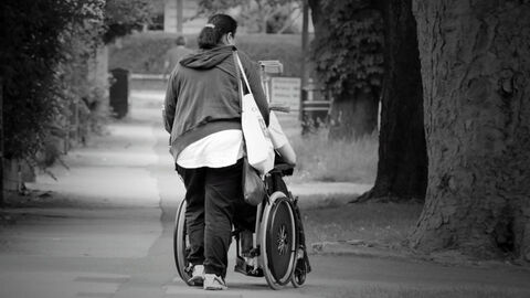 Junge Frau schiebt Rollstuhl.