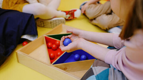 Kinder sitzen im Kreis und spielen mit einem Holzspielzeug.